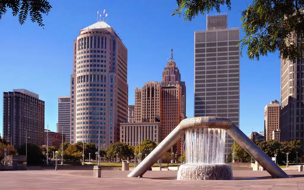 Hart Plaza in downtown Detroit featuring the Horace E. Dodge and Son Memorial Fountain surrounded by skyscrapers on a clear, sunny day.